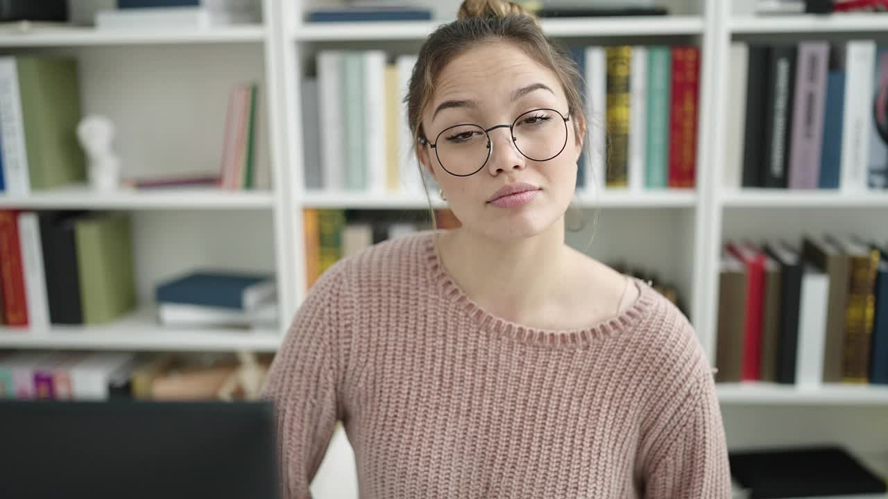 年轻漂亮的西班牙女学生用电脑做我不知道手势在图书馆大学视频素材