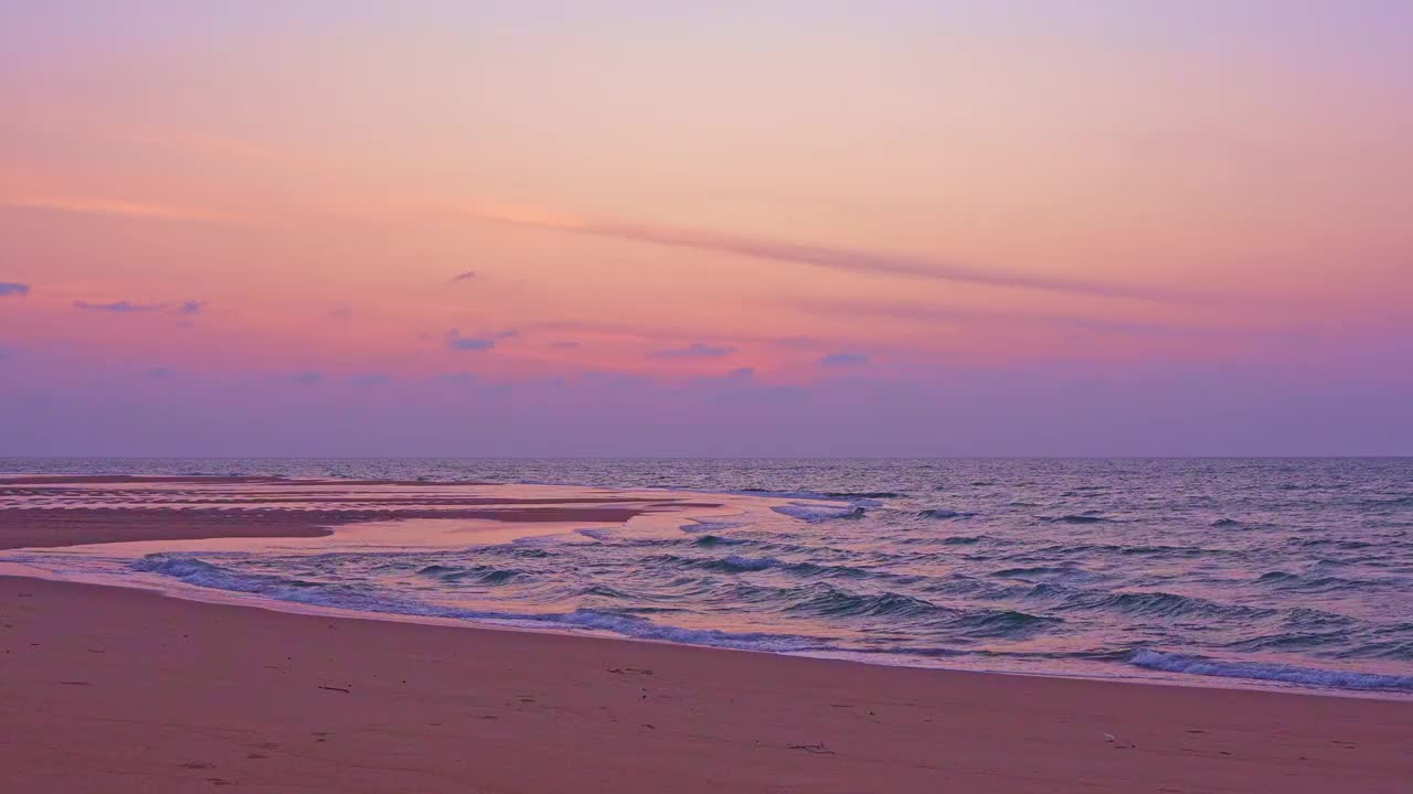 沙滩上金色的日落，泡沫般的海浪翻滚着冲向五彩缤纷的沙滩上的日落，美丽的日落或海上的日出，海浪撞击着海滩，五彩缤纷的天空视频素材