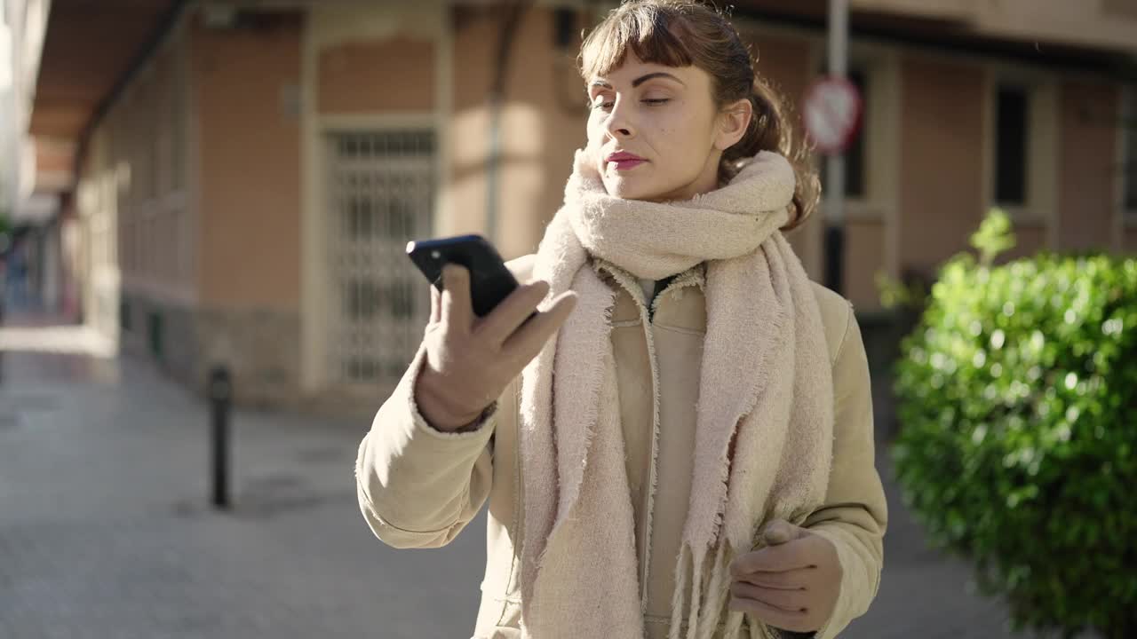 年轻的白人女子在街上用智能手机自拍视频素材