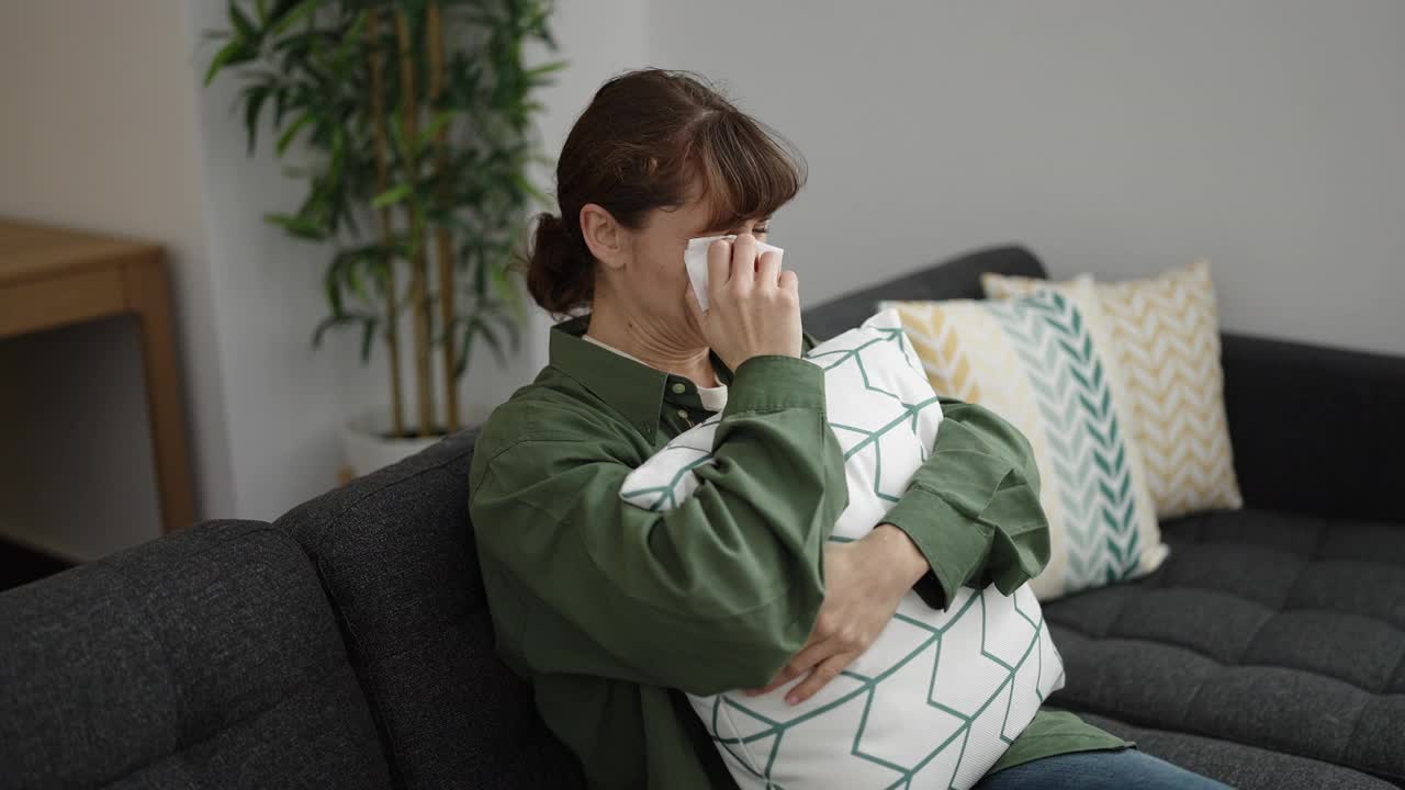 年轻的白人女子坐在沙发上抱着枕头哭泣视频素材