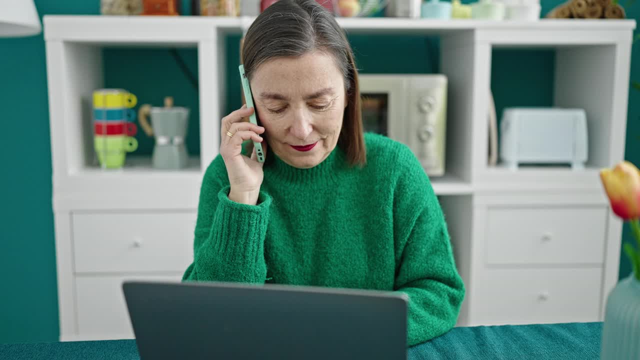 成熟的西班牙女子与灰色头发使用笔记本电脑在餐厅打电话视频素材