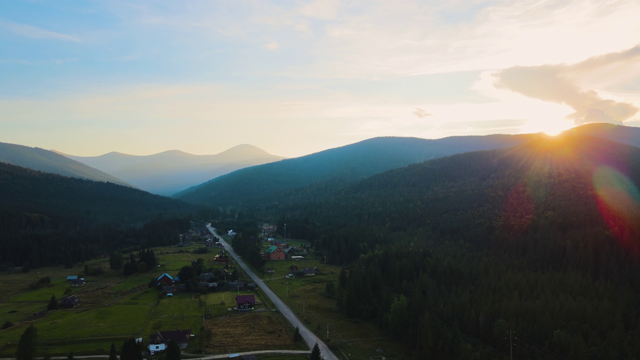 傍晚雾蒙蒙的鸟瞰图，在明亮的夕阳下，在高高的山峰之间的小山村的房子和深色的松林。黄昏时分野山林地的迷人景色视频素材