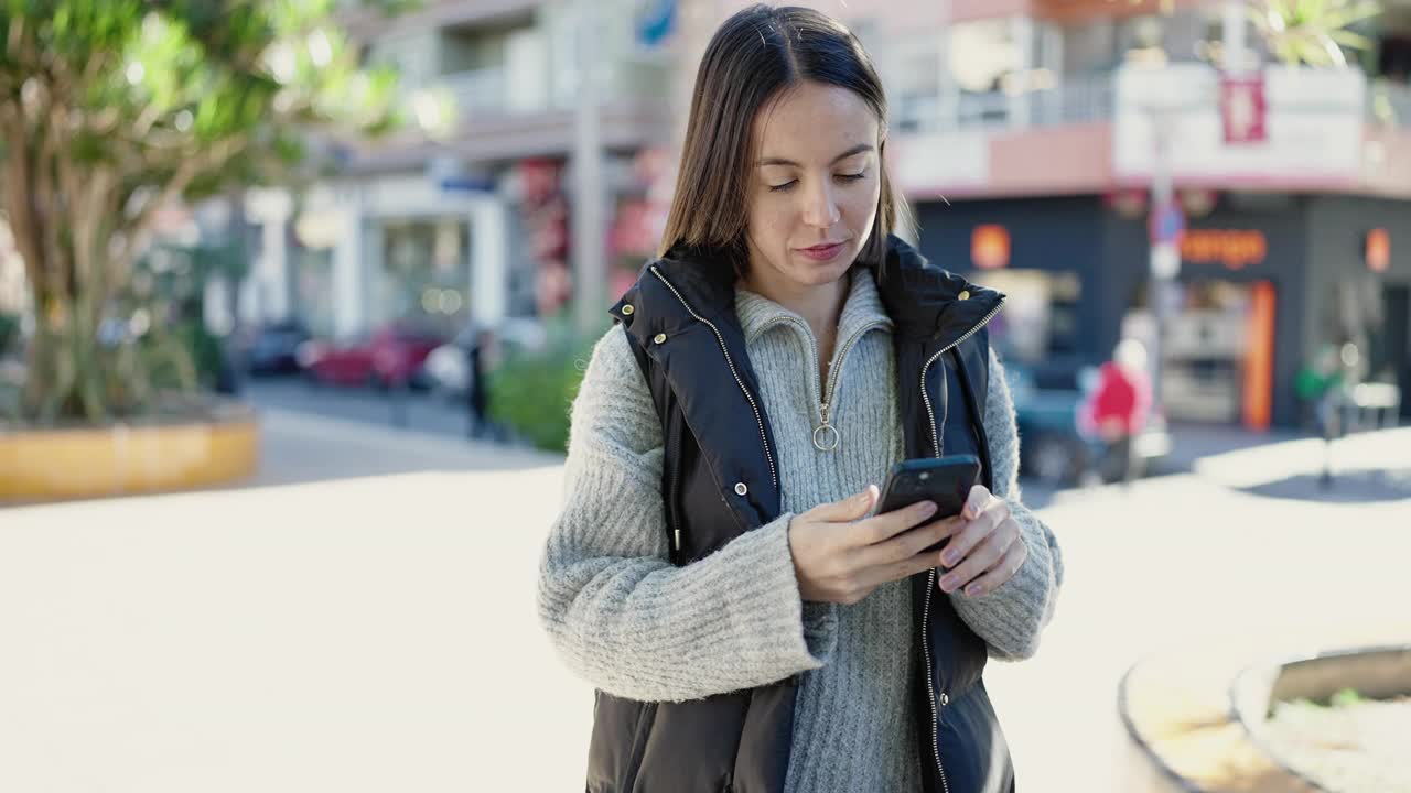 年轻美丽的西班牙女子在街上用智能手机微笑自信视频素材