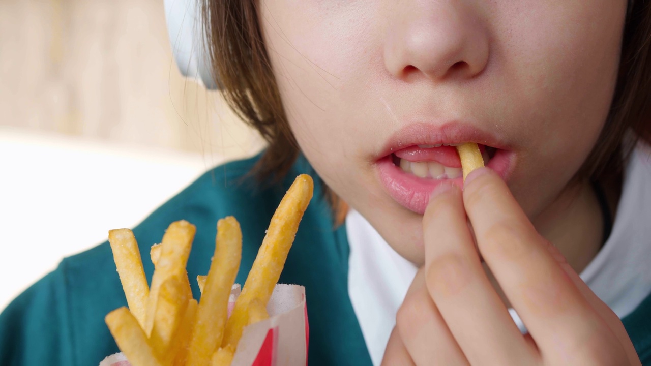 十几岁的女孩吃快餐薯条。青少年对垃圾食品上瘾。视频素材