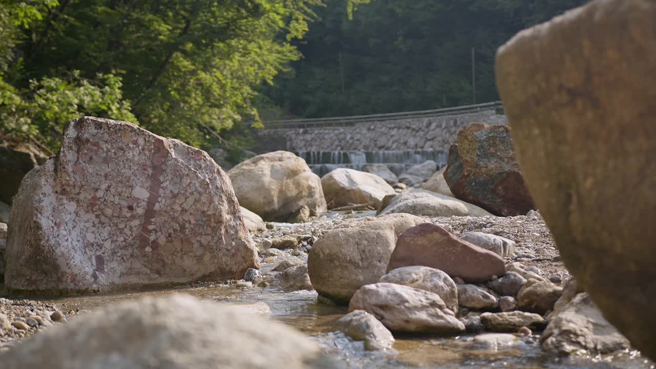 徒步旅行者，一个男人和一个女人跳过一条在岩石间流动的小溪，后视图视频素材