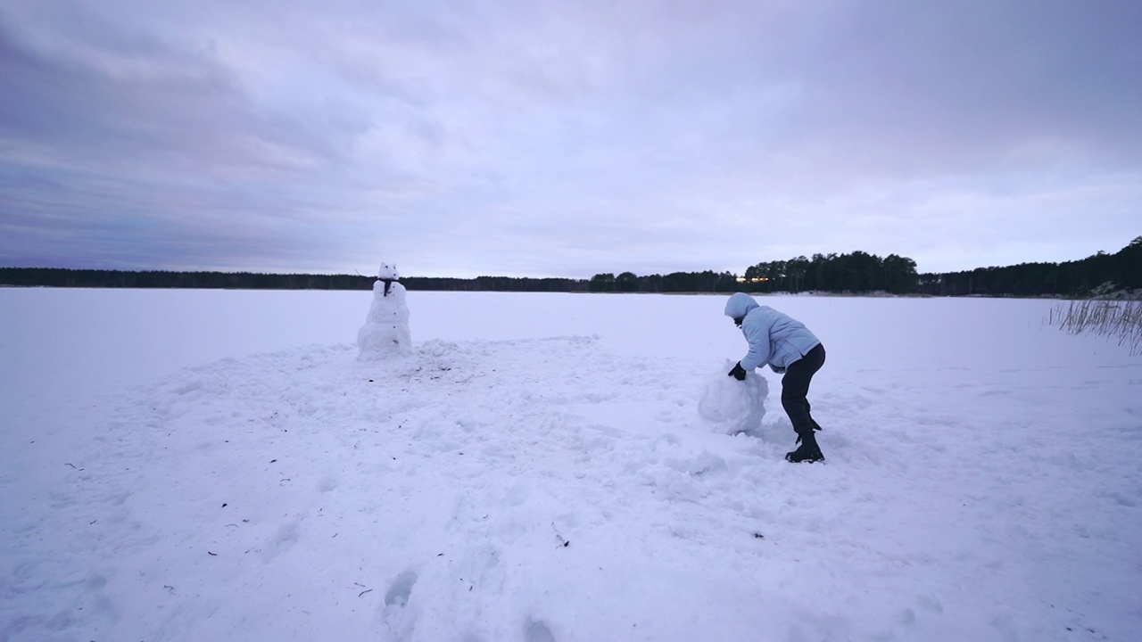 一名女子在冰湖岸边雕刻雪人视频素材