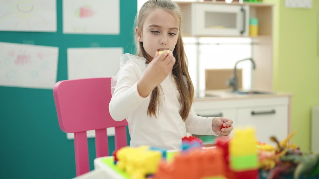 可爱的西班牙女孩坐在幼儿园的桌子上玩积木视频素材