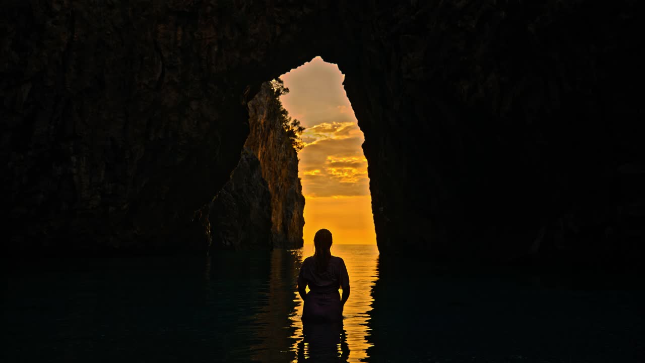 女人在她上方泼水，背景是美丽的天然拱门Spiaggia dell'Arcomagno。一个女人在意大利的旅行中玩得很开心。视频素材