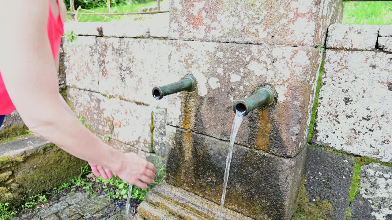 一名女子在古老的喷泉中用泉水洗手视频素材