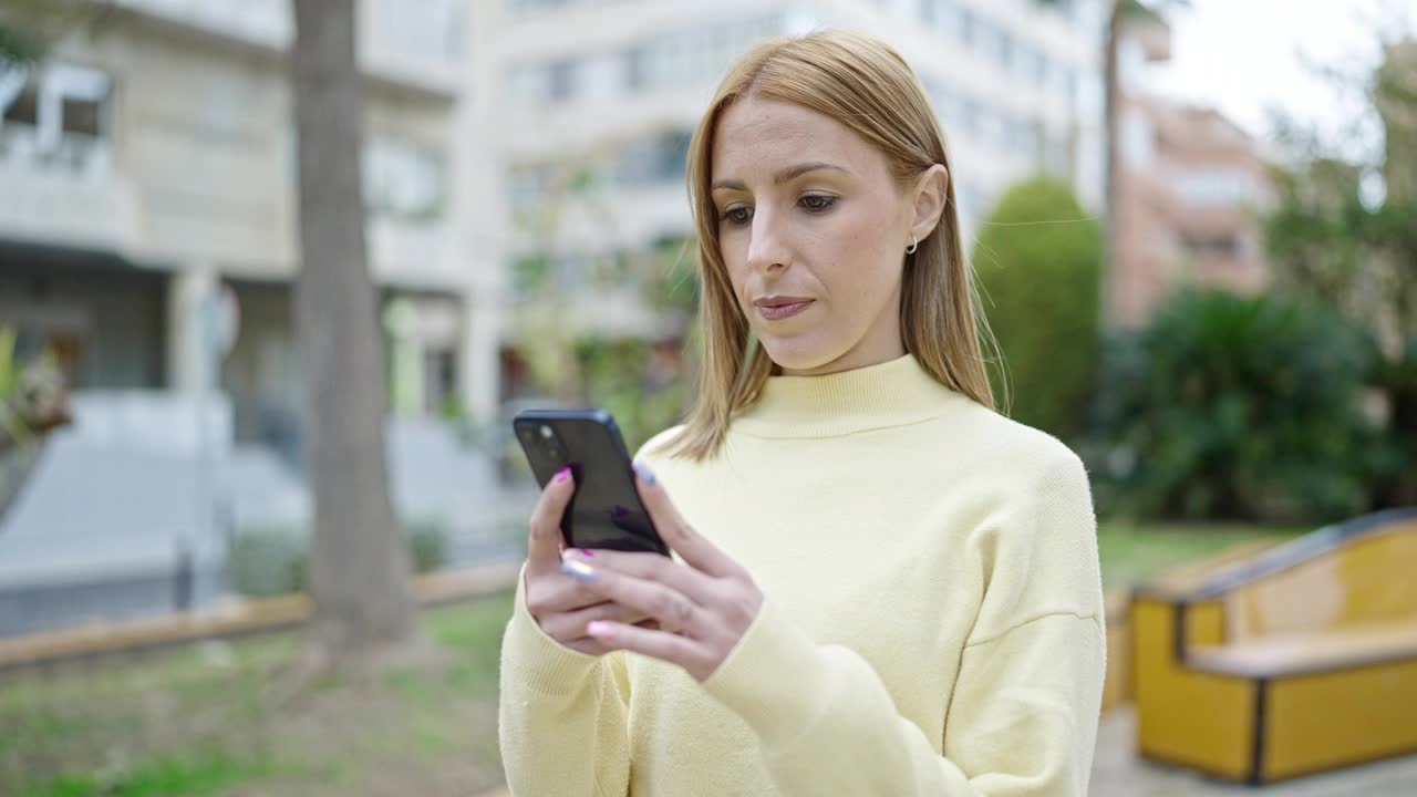 年轻的金发女子在公园里严肃地使用智能手机视频素材