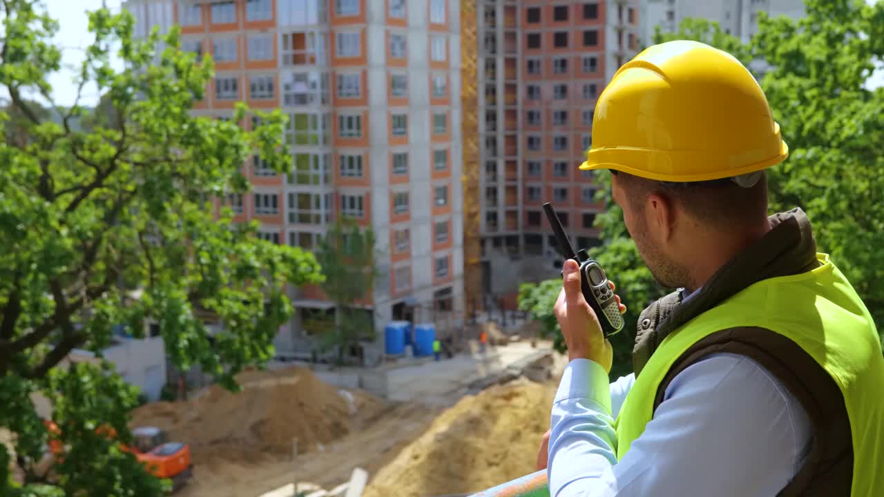 戴安全帽的男工头站在工地，通过对讲机进行指导。建筑工人的手势和竖起大拇指。实时视频视频素材