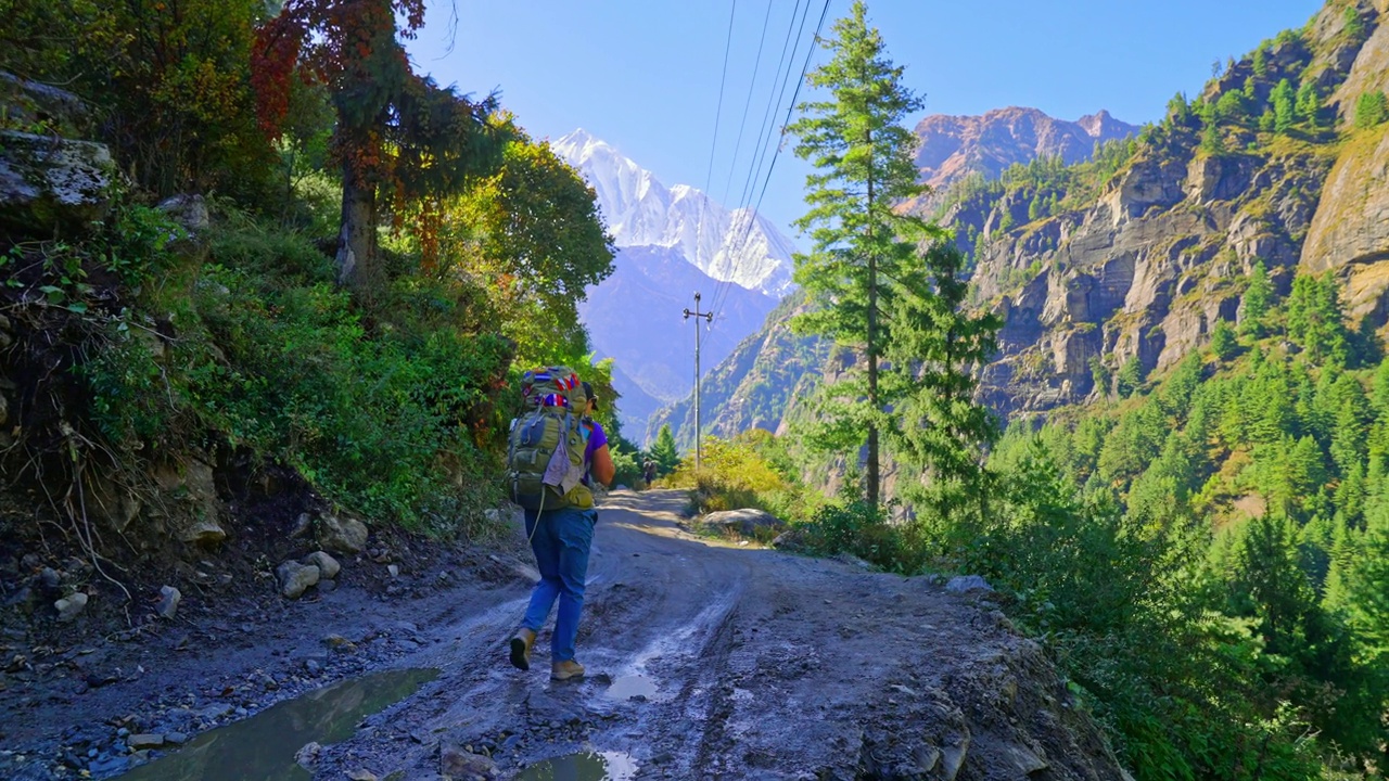 徒步旅行者走在泥泞的小路上，陡峭的悬崖和雪山一览无垠的自然风光，尼泊尔安纳普尔纳环行视频素材