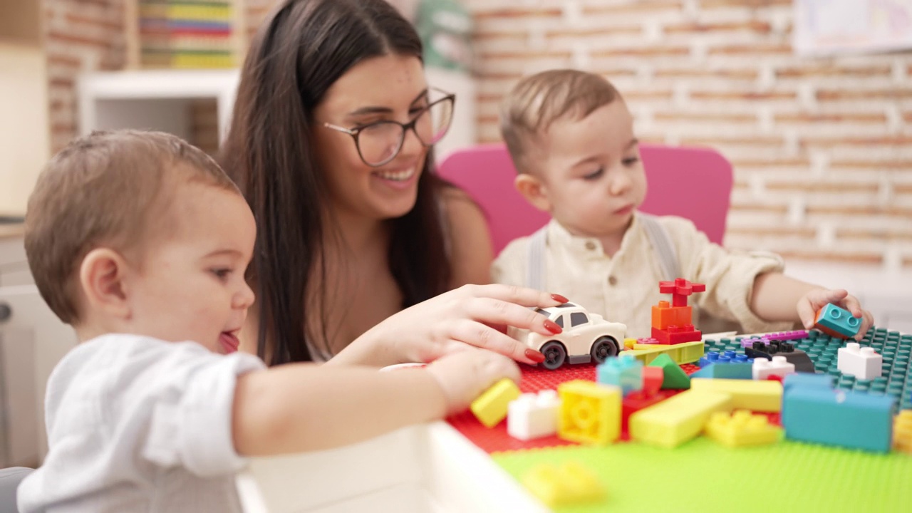 幼儿园里，老师和坐在桌子上玩积木的男孩们在一起视频素材