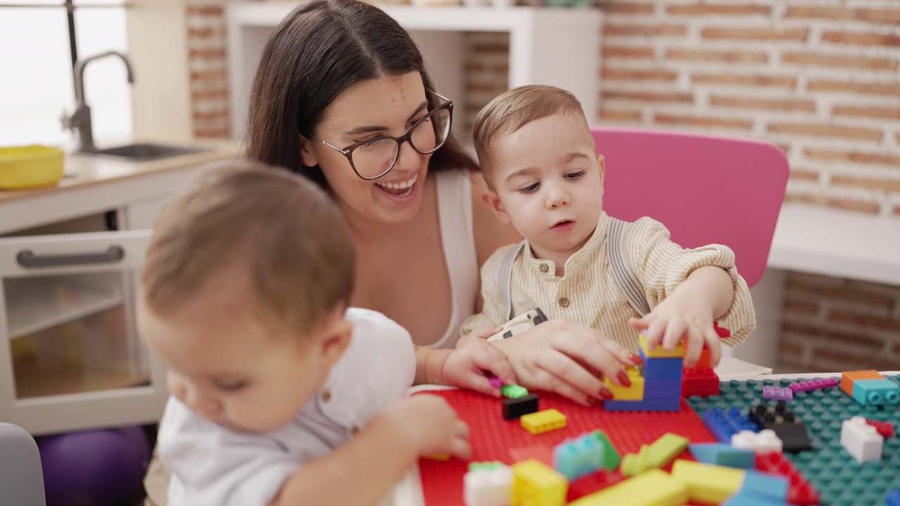 幼儿园里，老师和坐在桌子上玩积木的男孩们在一起视频素材