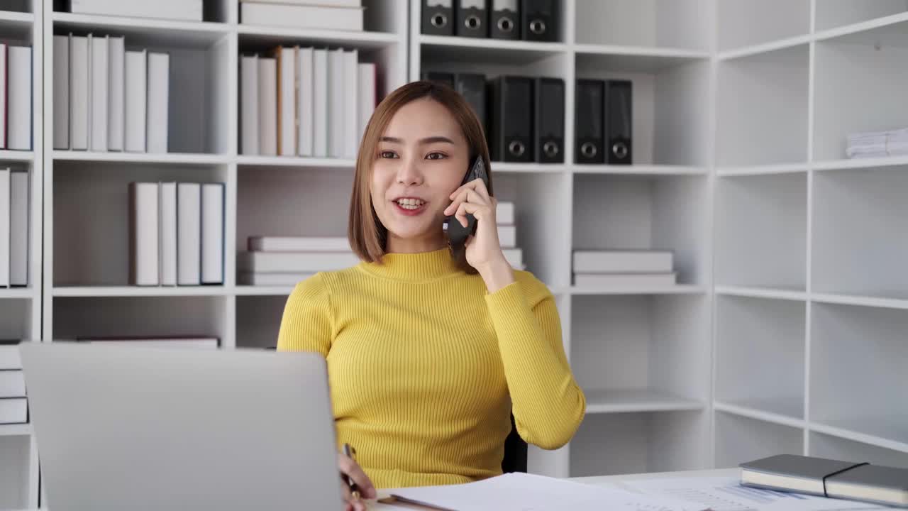 有魅力的职业女性员工在工作场所坐在桌子上，用手机聊天，与同事交流。视频素材