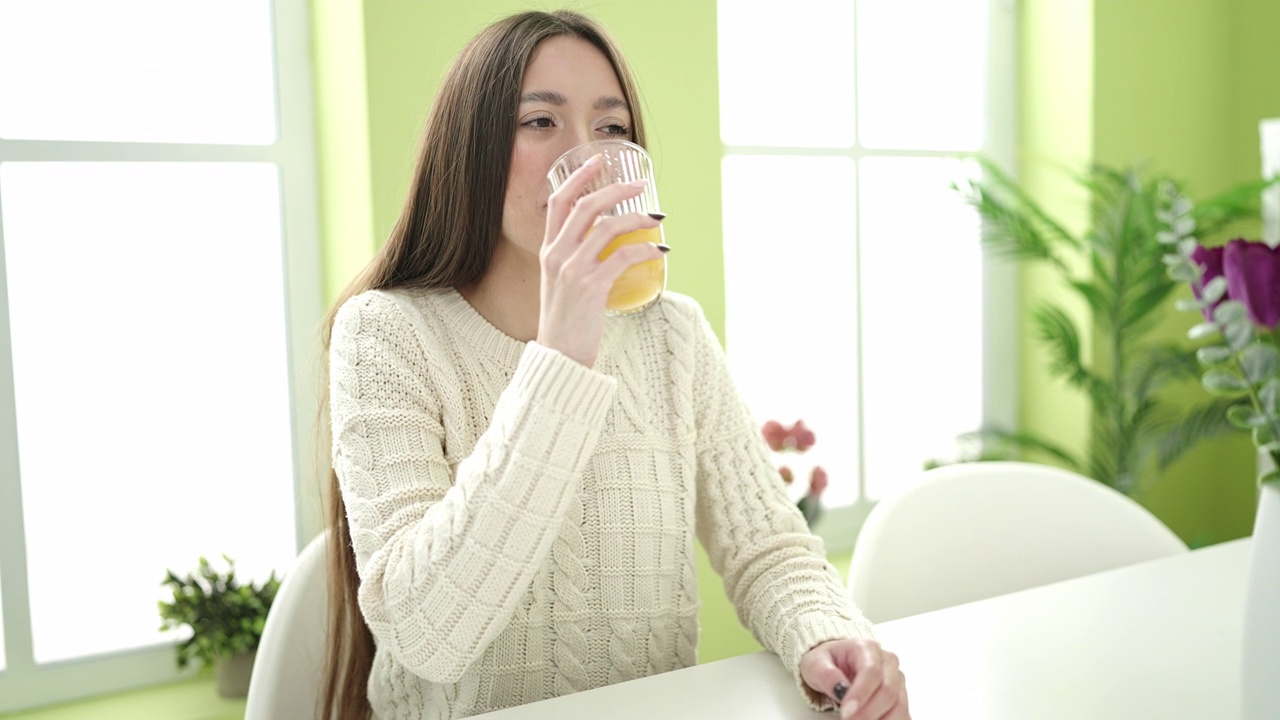 年轻美丽的西班牙女子喝着一杯橙汁坐在家里的桌子上视频素材