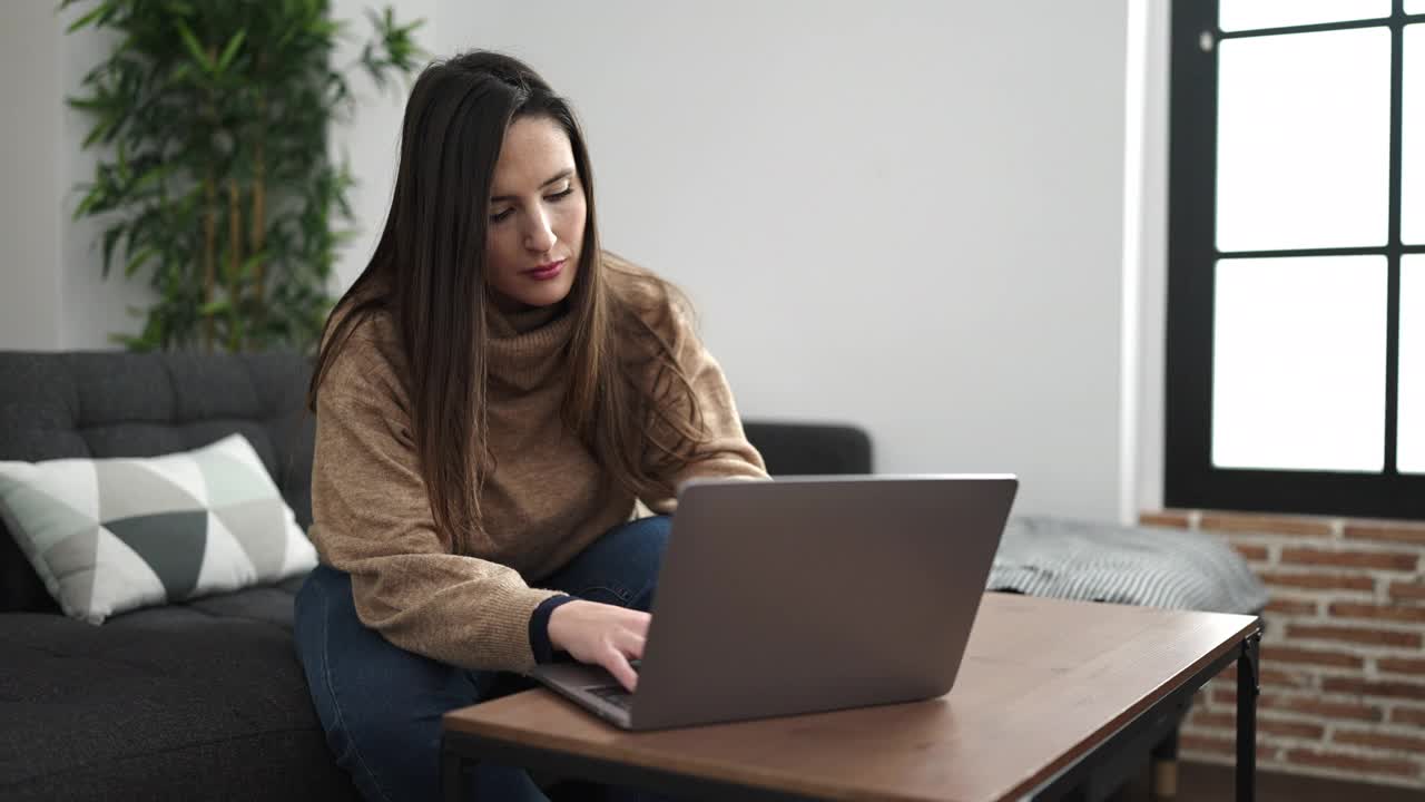 美丽的西班牙女子使用笔记本电脑坐在沙发上，在家里担心的表情视频素材