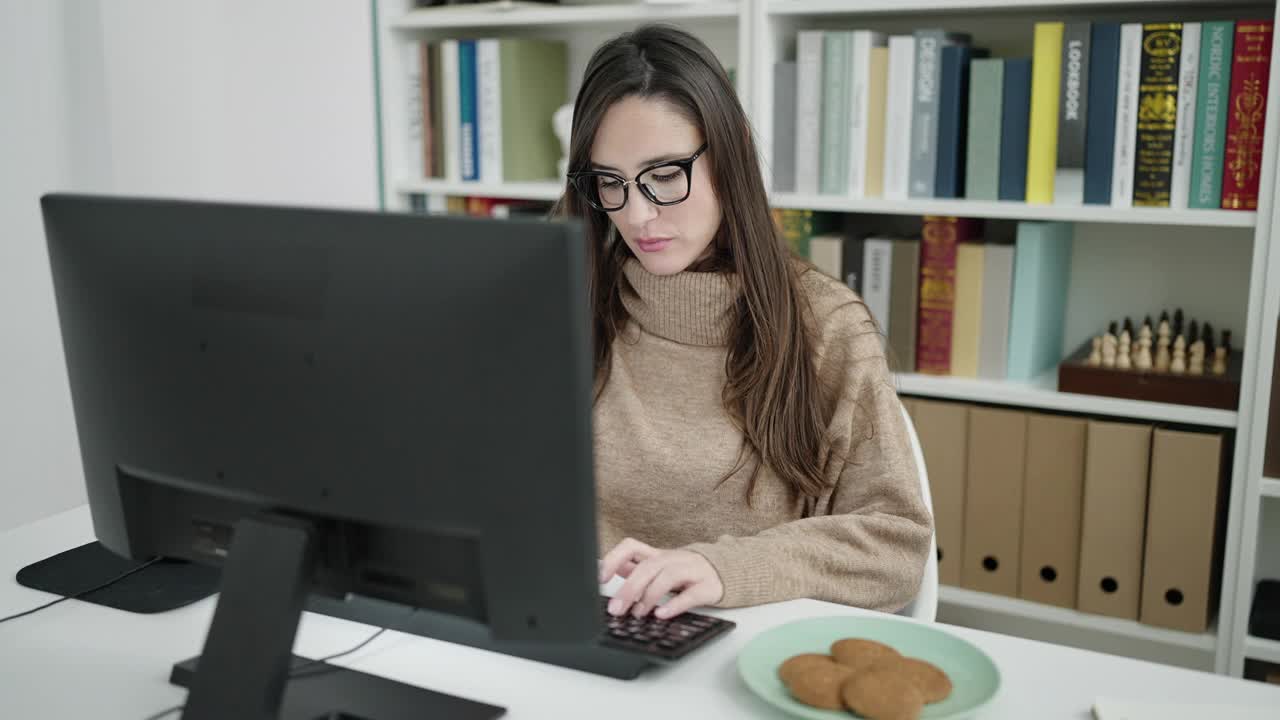 美丽的西班牙女学生使用电脑吃饼干在图书馆大学视频素材