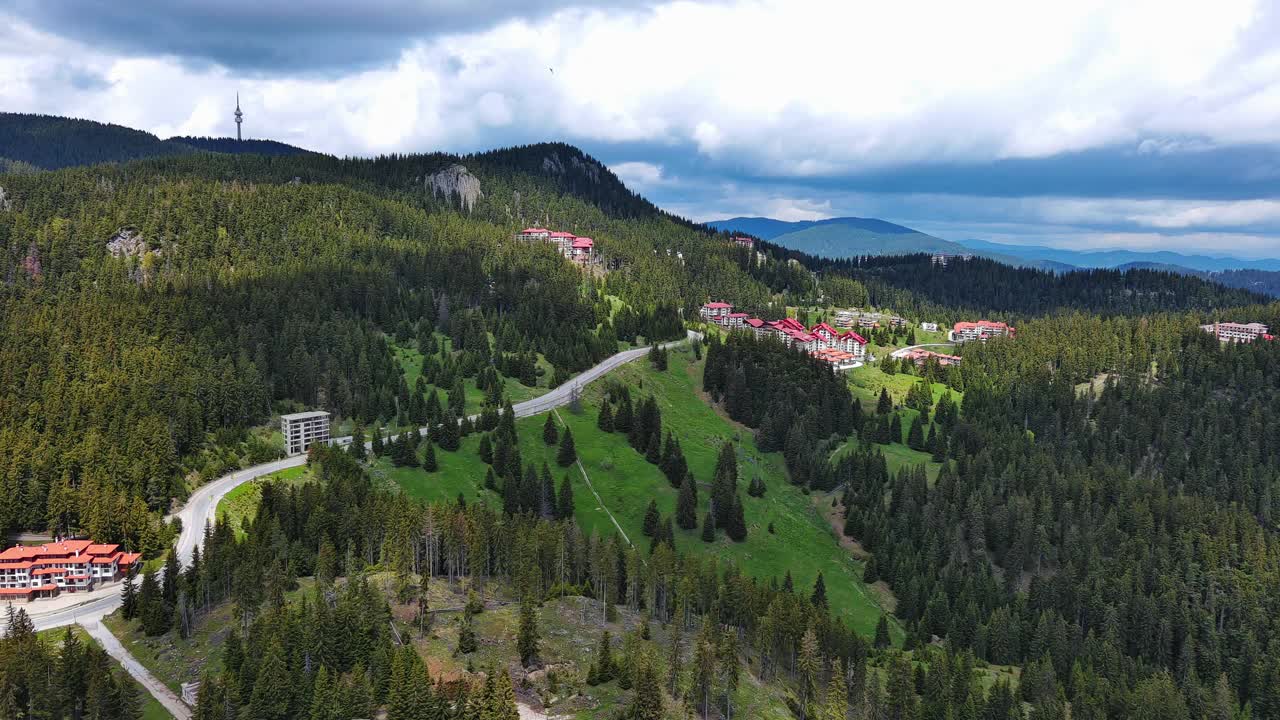 一条路经过布满云杉森林和草地的山丘，映衬着多云的天空视频素材