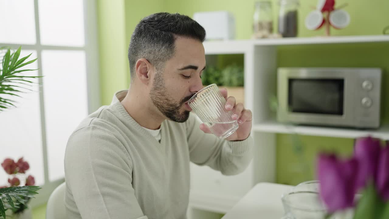 年轻的西班牙人坐在家里的桌子上喝水视频素材