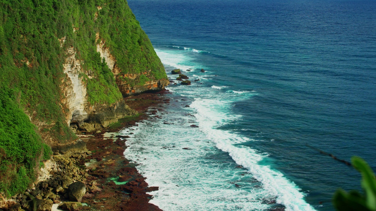 原始的太平洋海浪泡沫和巴厘岛海滩的自然景观。郁郁葱葱的异国情调的绿色植物和蓝色的大海。风景如画的海岸上，阳光明媚。Uluwatu。视频素材