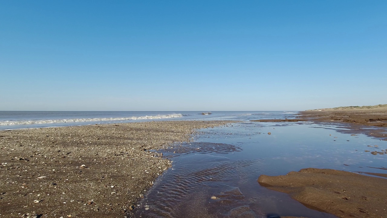 宁静的夏季4K海滩场景，展示了清澈的海水穿过沙滩的宁静流动，平静的海洋潮汐，以及适合休闲度假或旅游的海岸景观视频素材