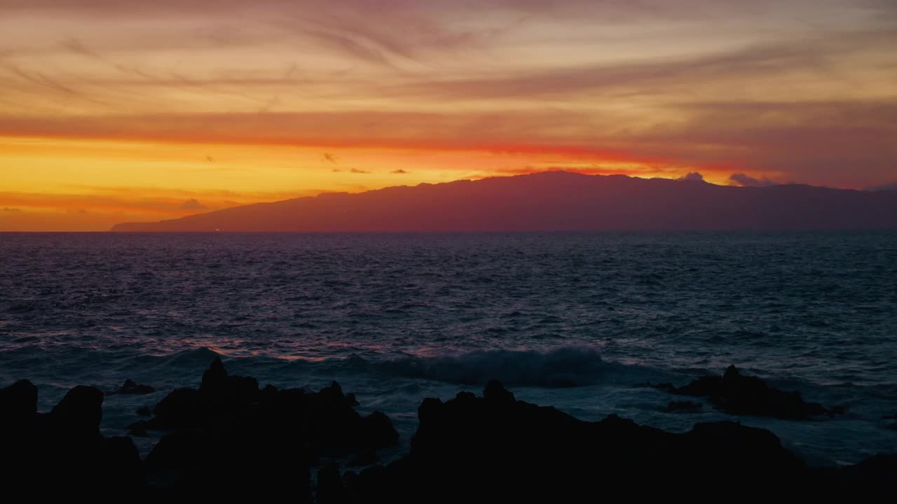 明亮的橙色日落夜空，海洋和飞翔的候鸟群。岩石火山海滩，黑色海浪。视频素材