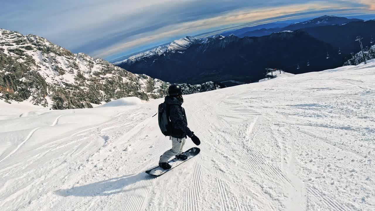 单板滑雪的艺术:一个才华横溢的骑手在冬季的仙境中雕刻他的路，在他的身后留下一串新鲜的粉雪，在灿烂的阳光和山脉的蓝天下视频素材