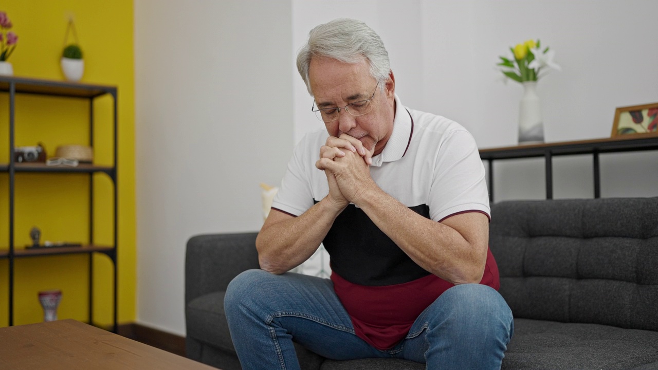 白发苍苍的中年男子坐在家里的沙发上，感到很紧张视频素材