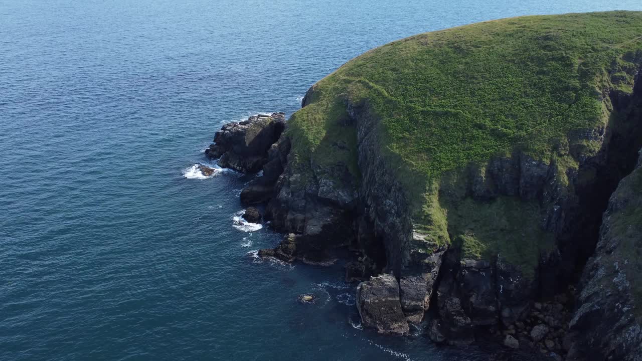 航拍视频显示，海浪拍打着长满绿草的岩石海岸视频素材