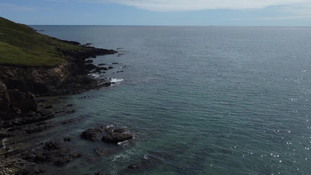 航拍视频显示，海浪拍打着长满绿草的岩石海岸视频素材