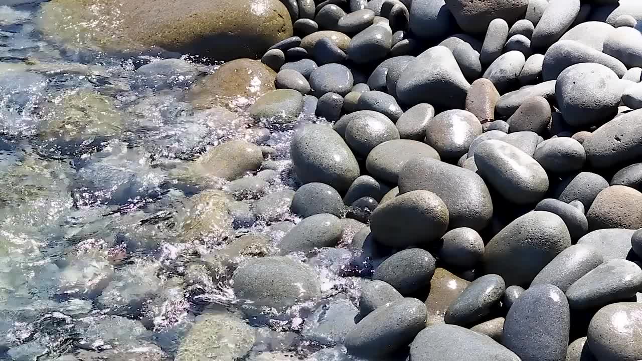 在白天，海浪溅在透明的海水海岸上的石头上的特写视频素材