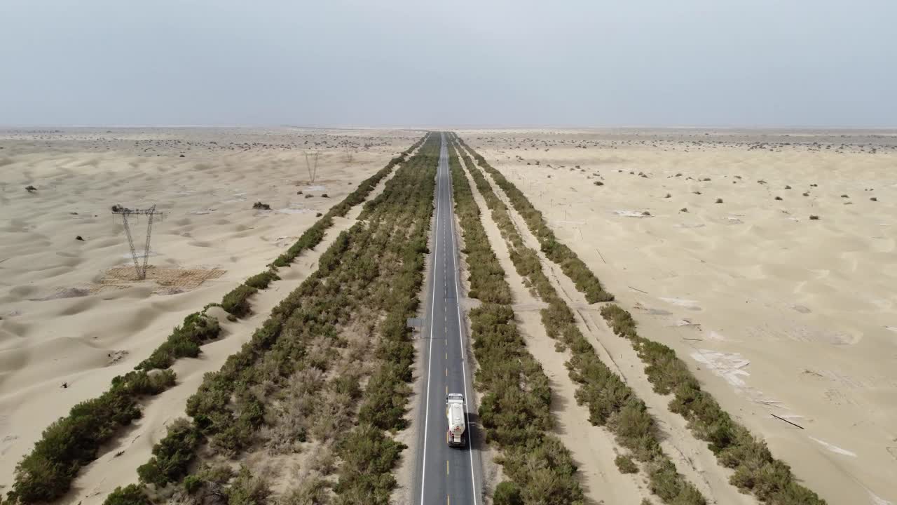 航拍视频显示，一辆汽车行驶在沙漠和树木环绕的道路上视频素材