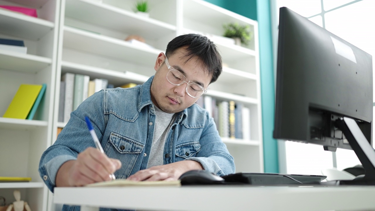 在图书馆大学，年轻的中国男学生正在用电脑在笔记本上写字视频素材