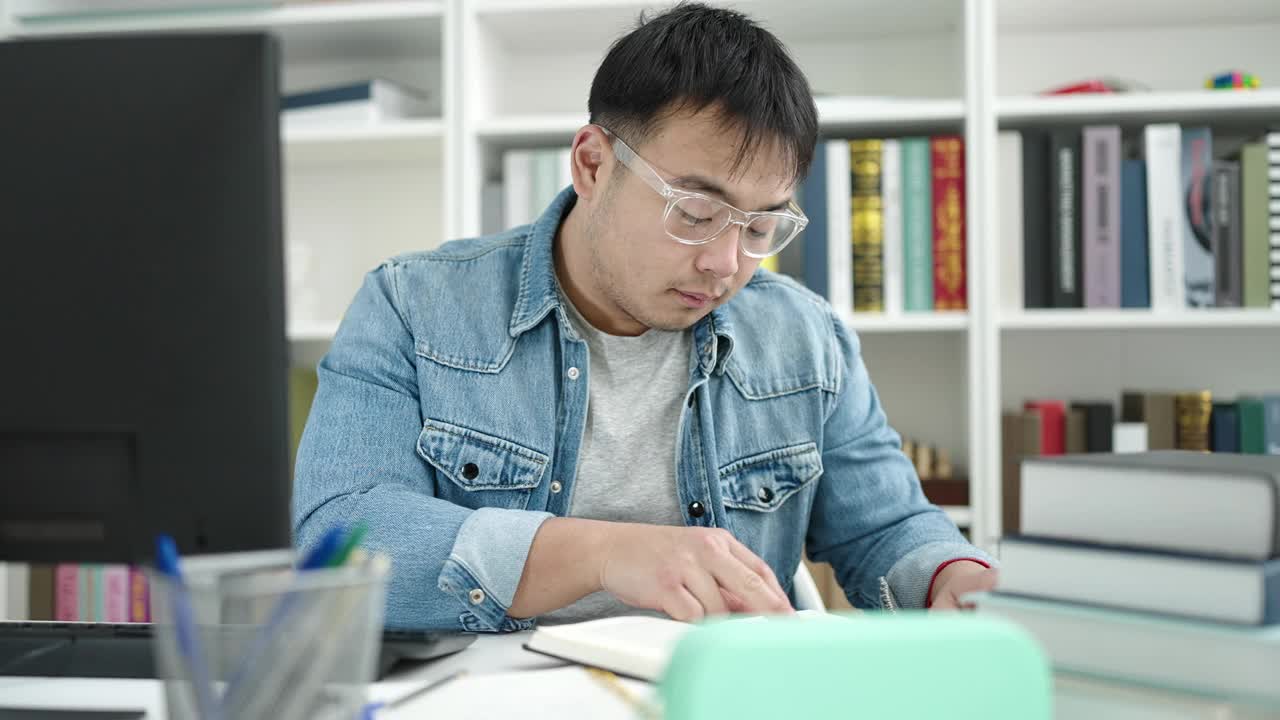 年轻的中国男学生坐在图书馆大学的桌子上看书视频素材