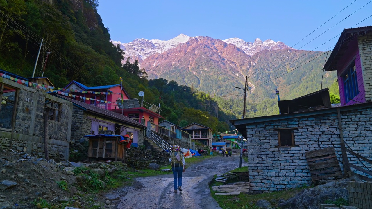 徒步旅行者进入喜马拉雅山脉小村庄的街景，远处有雪山，尼泊尔安纳普尔纳视频素材