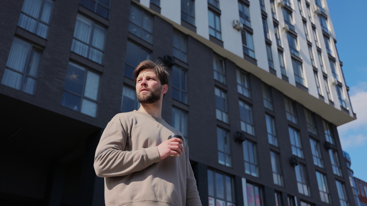 英俊的年轻白人男子手持纸杯在现代建筑的背景。视频素材