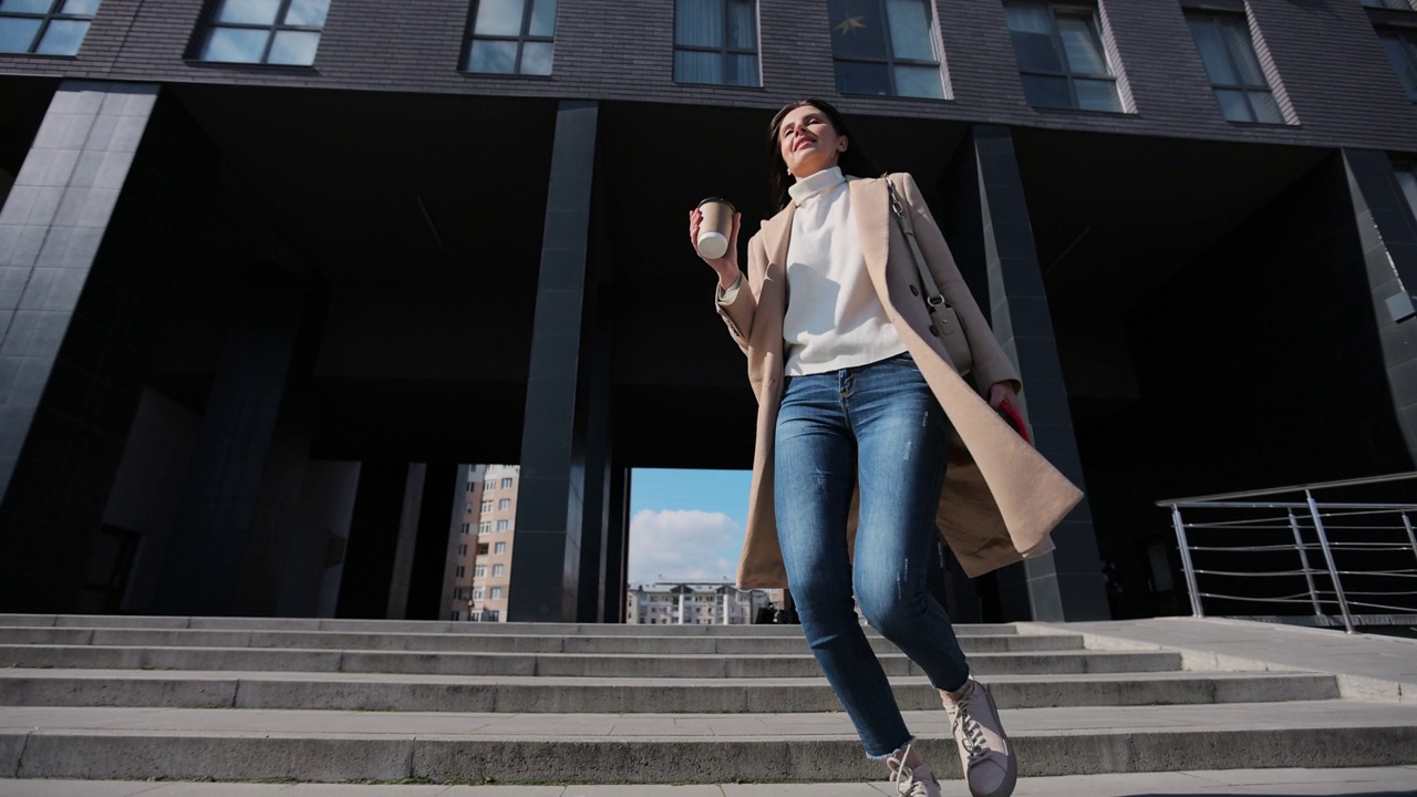 成功有魅力的女人喝着外卖咖啡在街上跑下楼梯。女商人喝着咖啡出门。后台办公中心。视频素材