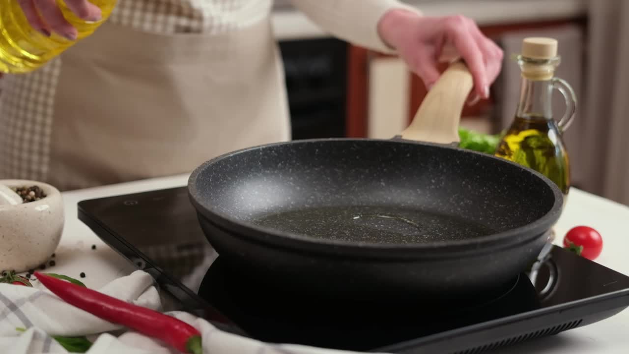 一位妇女把植物油倒进电磁炉上的煎锅里视频素材