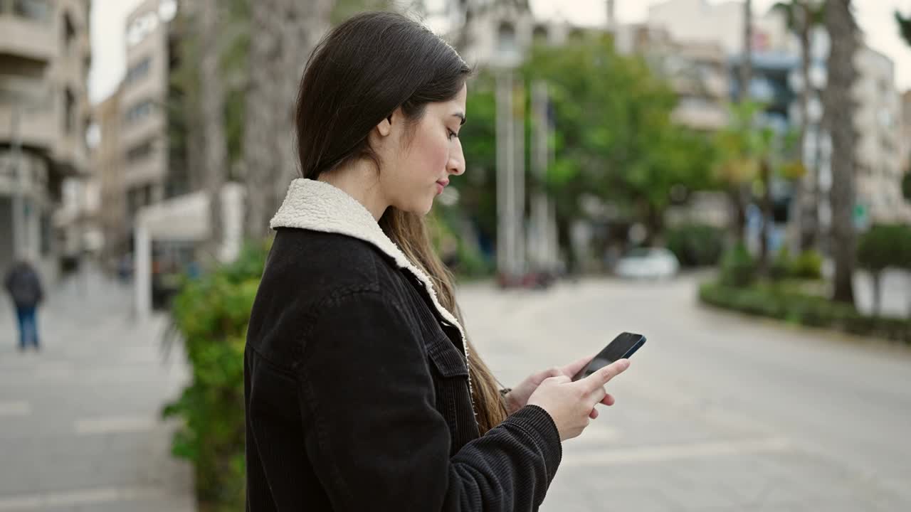 年轻美丽的西班牙女子在公园里用智能手机自信地微笑着视频素材