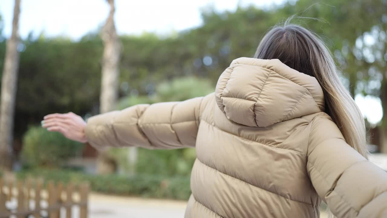 年轻的金发女子微笑着自信地站在公园里，双臂张开视频素材