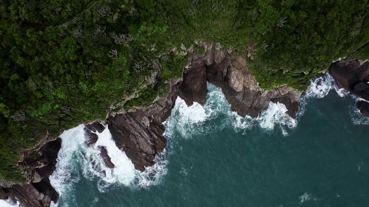 无人机飞过绿色的岩石峭壁，海浪飞溅视频素材