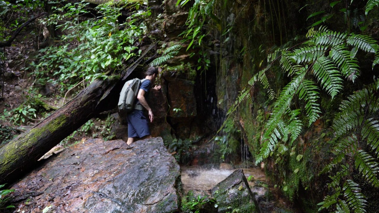 一位徒步旅行者在雨林中的小瀑布下洗脸视频素材