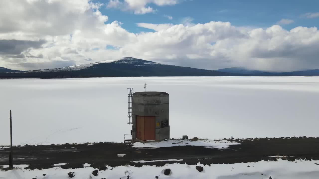 在多云的天空下，一个冰冻的水库与雪山的背景视频素材