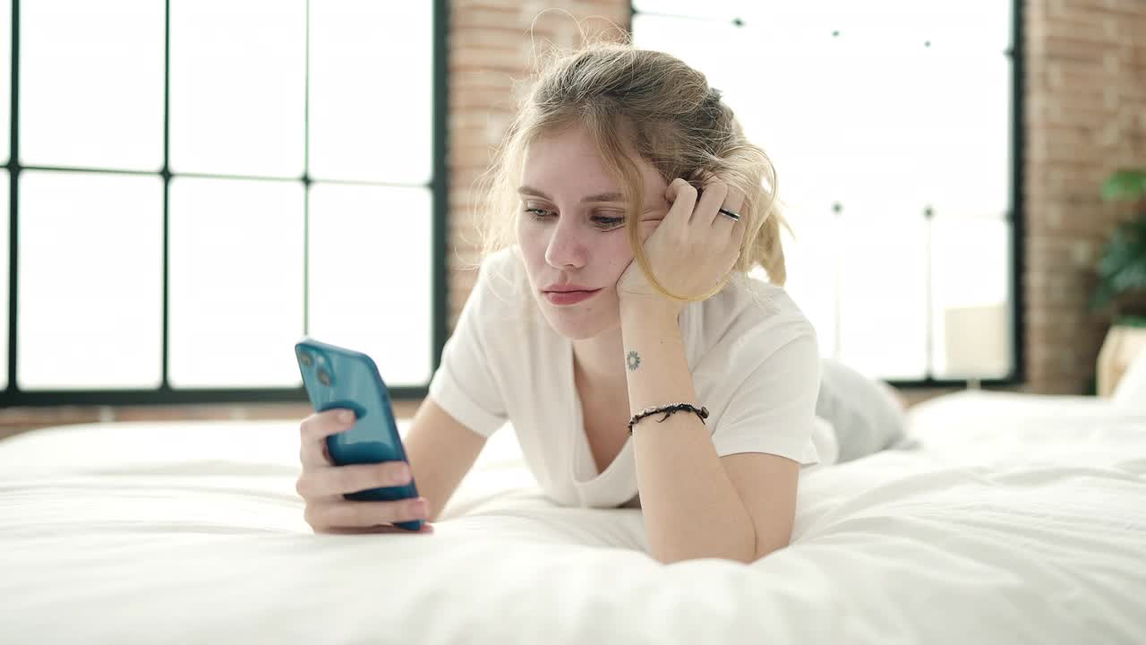 年轻的金发女子在卧室里用着智能手机，一脸不开心视频素材