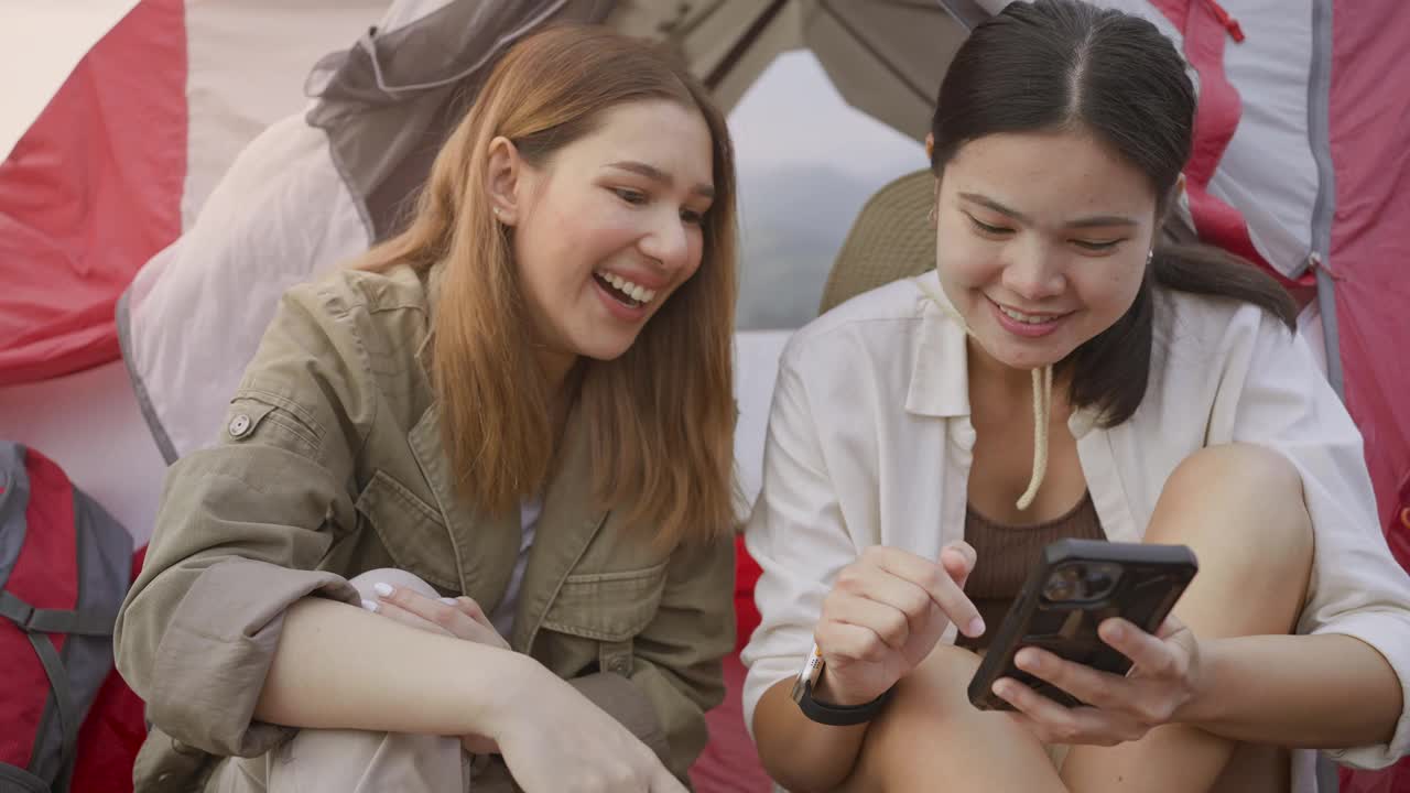 两个亚洲年轻女性是朋友，她们在山上露营时一起使用智能手机。视频素材