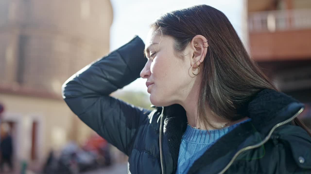 年轻的白人妇女站在街上，表情严肃，抚摸着头发视频素材