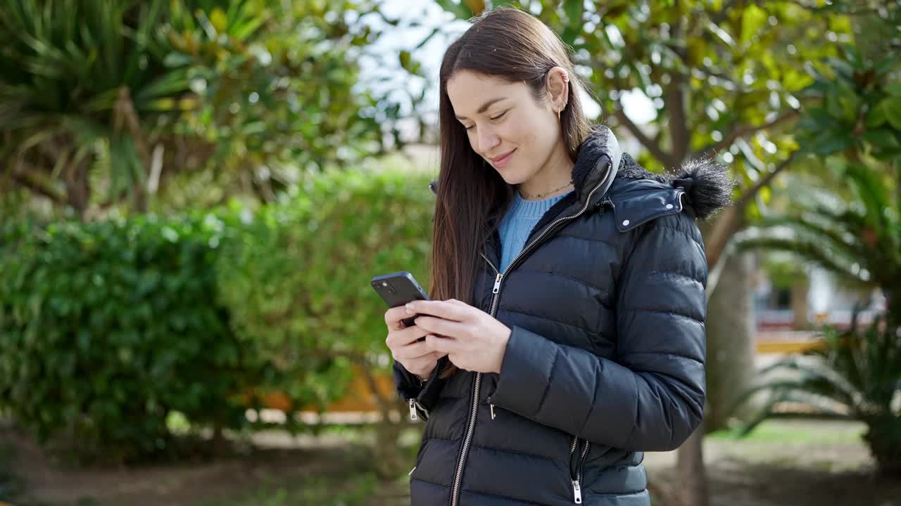 年轻的白人女子在公园用智能手机自信地微笑着视频素材