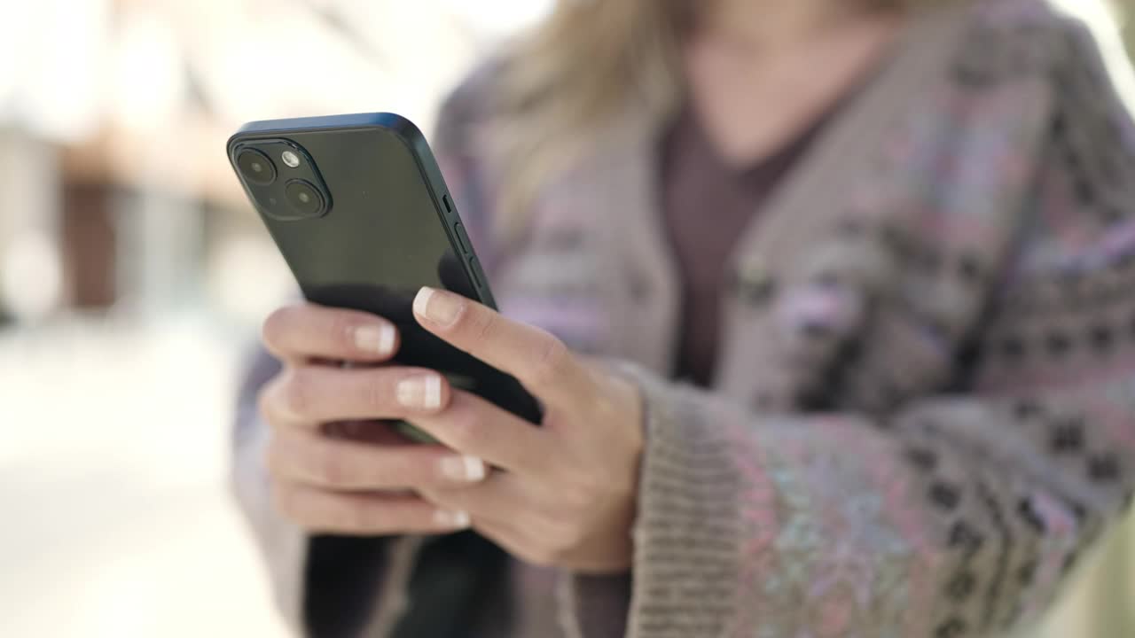 年轻的金发女子在街上使用智能手机视频素材