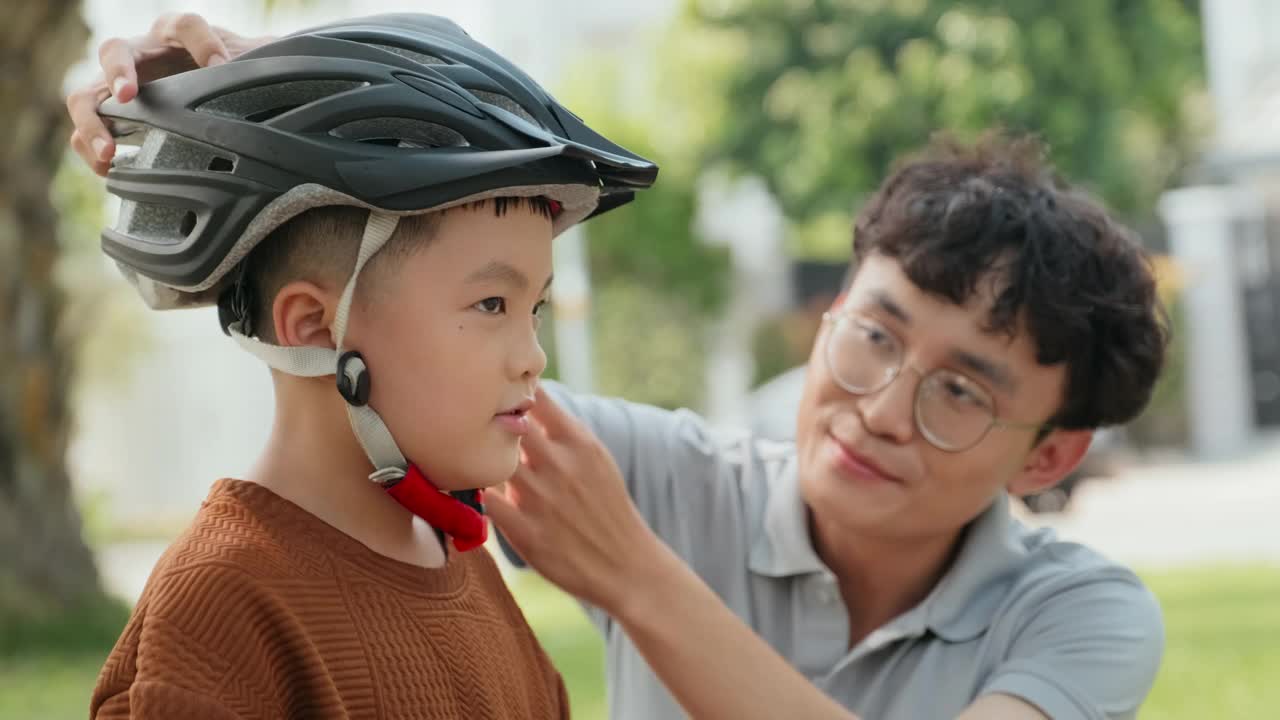 亚洲小孩在爸爸的帮助下在公园骑自行车视频素材